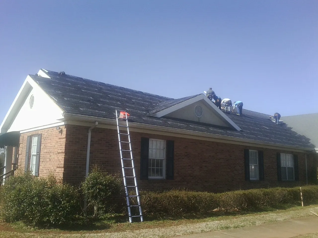 Crew tearing shingles off a brick ranch roof with a ladder set — Emergency Roof Repair work by our crew in Platina