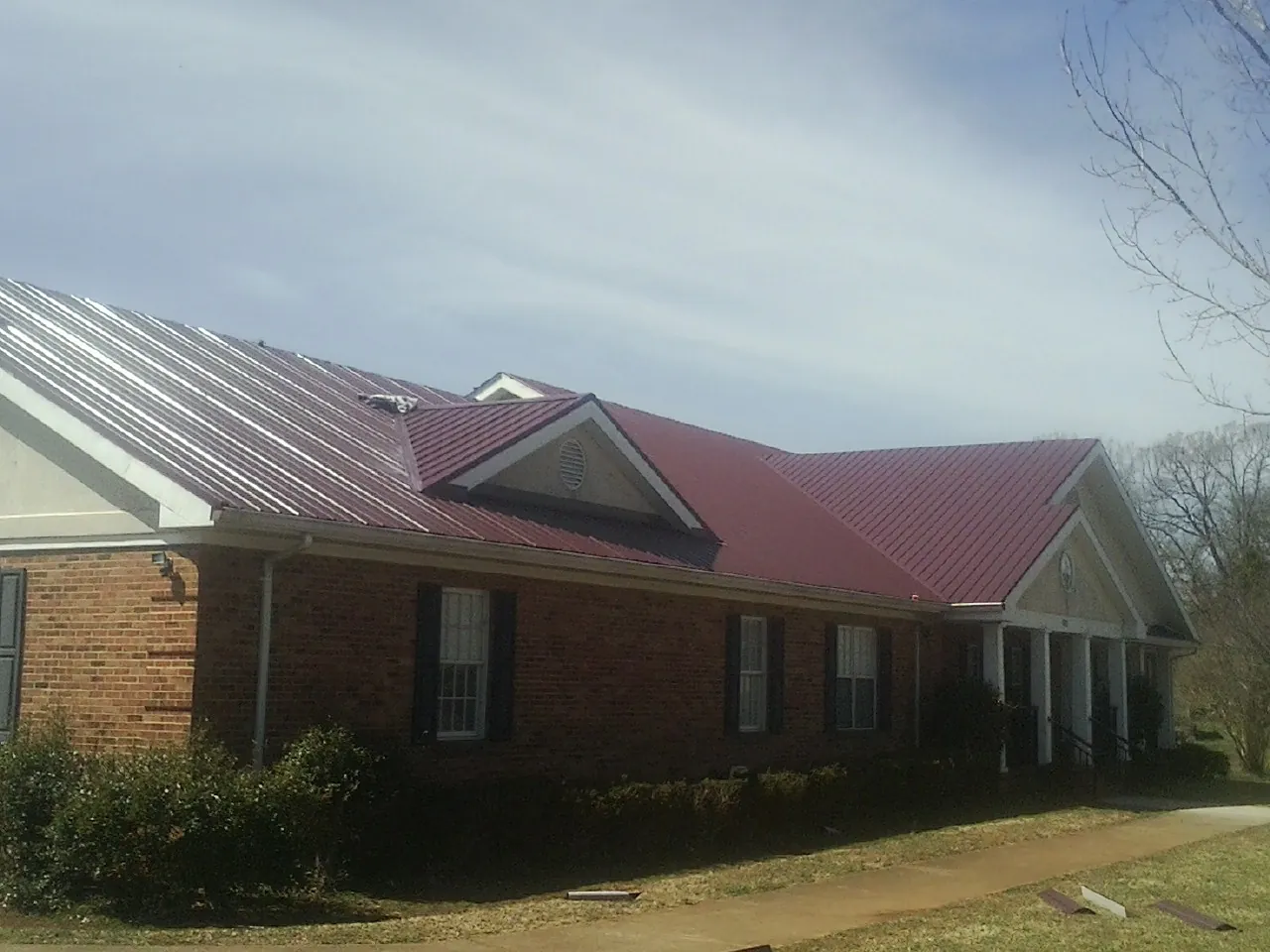 Red metal roof with gabled entries on a long brick building, from a Hail Damage Roof Repair job in Platina