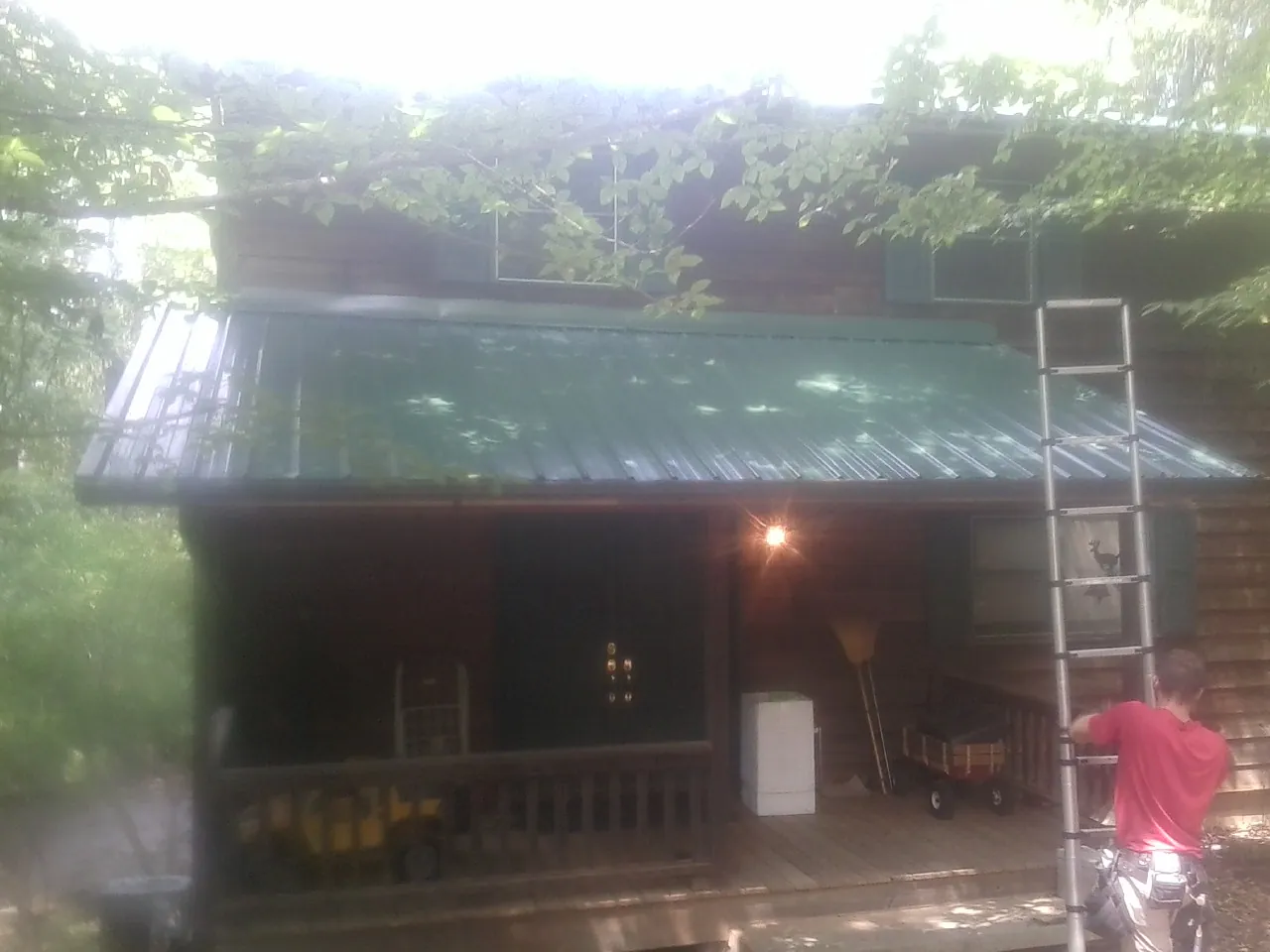 Worker on a ladder at the green porch roof of a wooded cabin in Platina