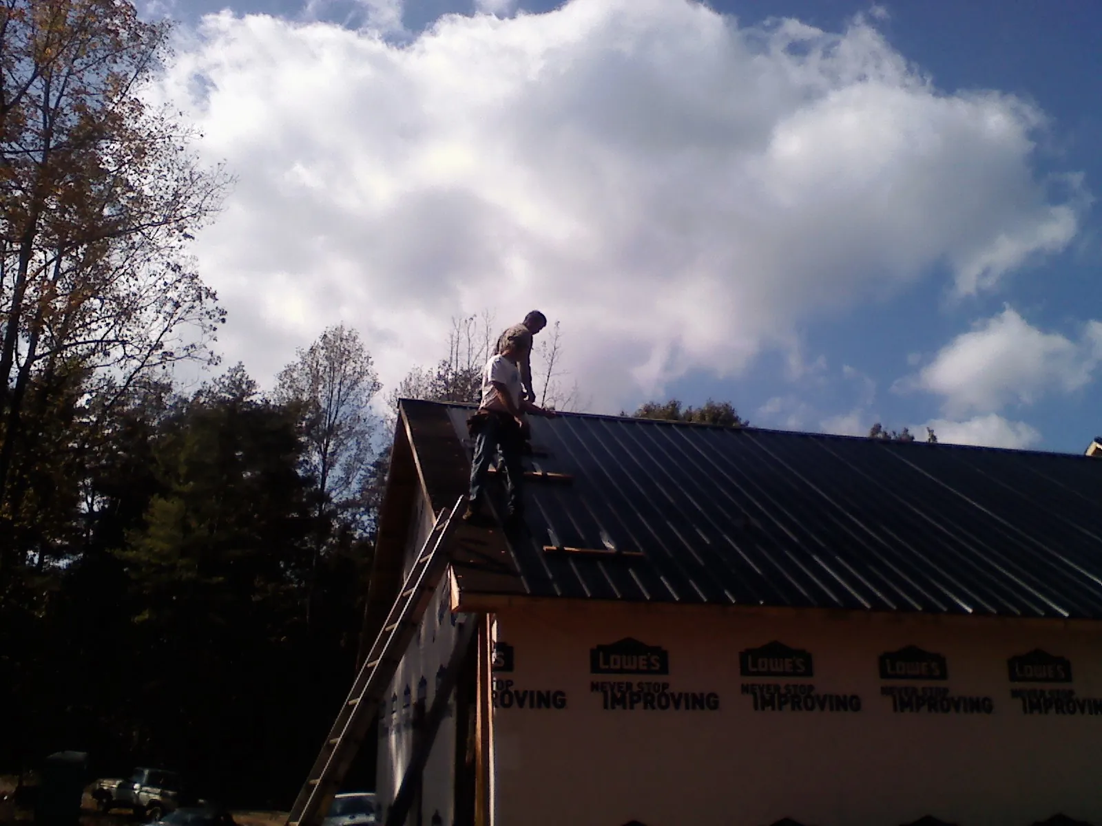Roofer fastening dark metal panels high against a cloudy sky, from a Roof Inspection job in Platina